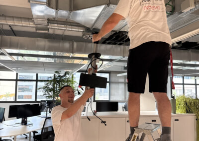 Two nesevo technicians mounting a ceiling-mounted device in an open-plan office